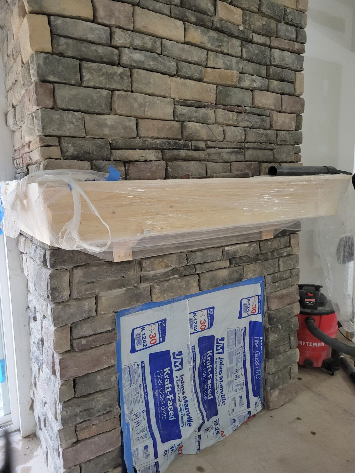 Stone fireplace with wood mantel under construction