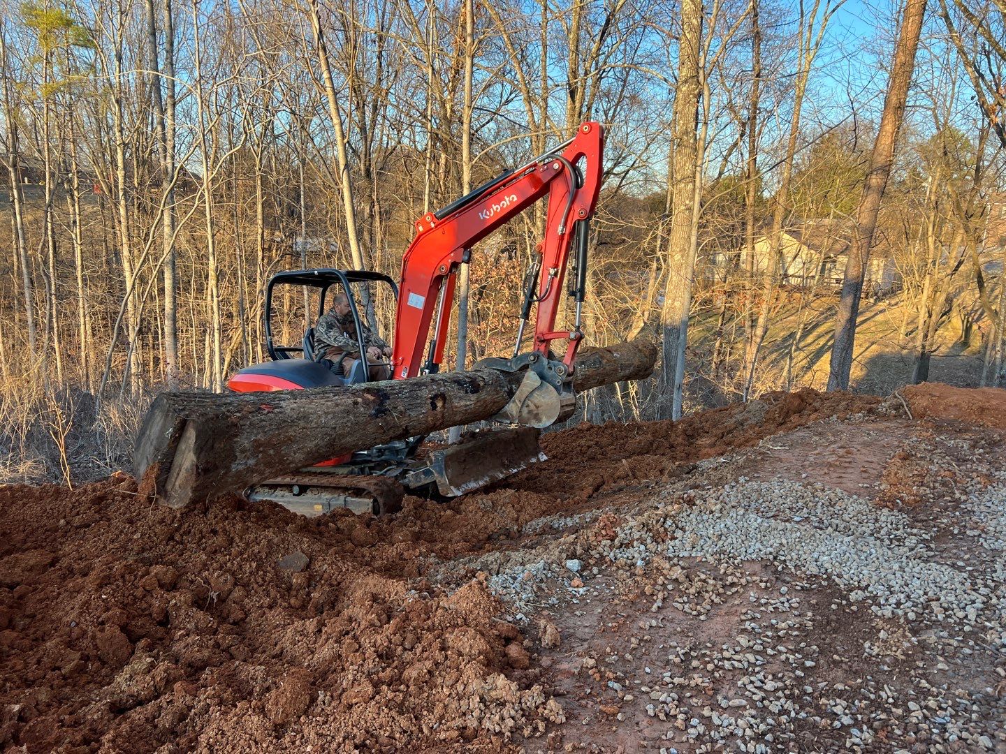 Kubota excavator moving logs on hillside
